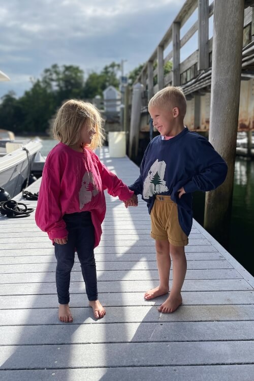 Rogue Life kids apparel - Two children holding hands on a dock by a body of water.
