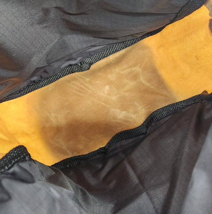 A picture of the inside of the wax Stella Bag. there is a black ripstop lining on the sides, with the inside layer of the wax fabric on the bottom. All the raw edges have been binded with gross grain ribbon.